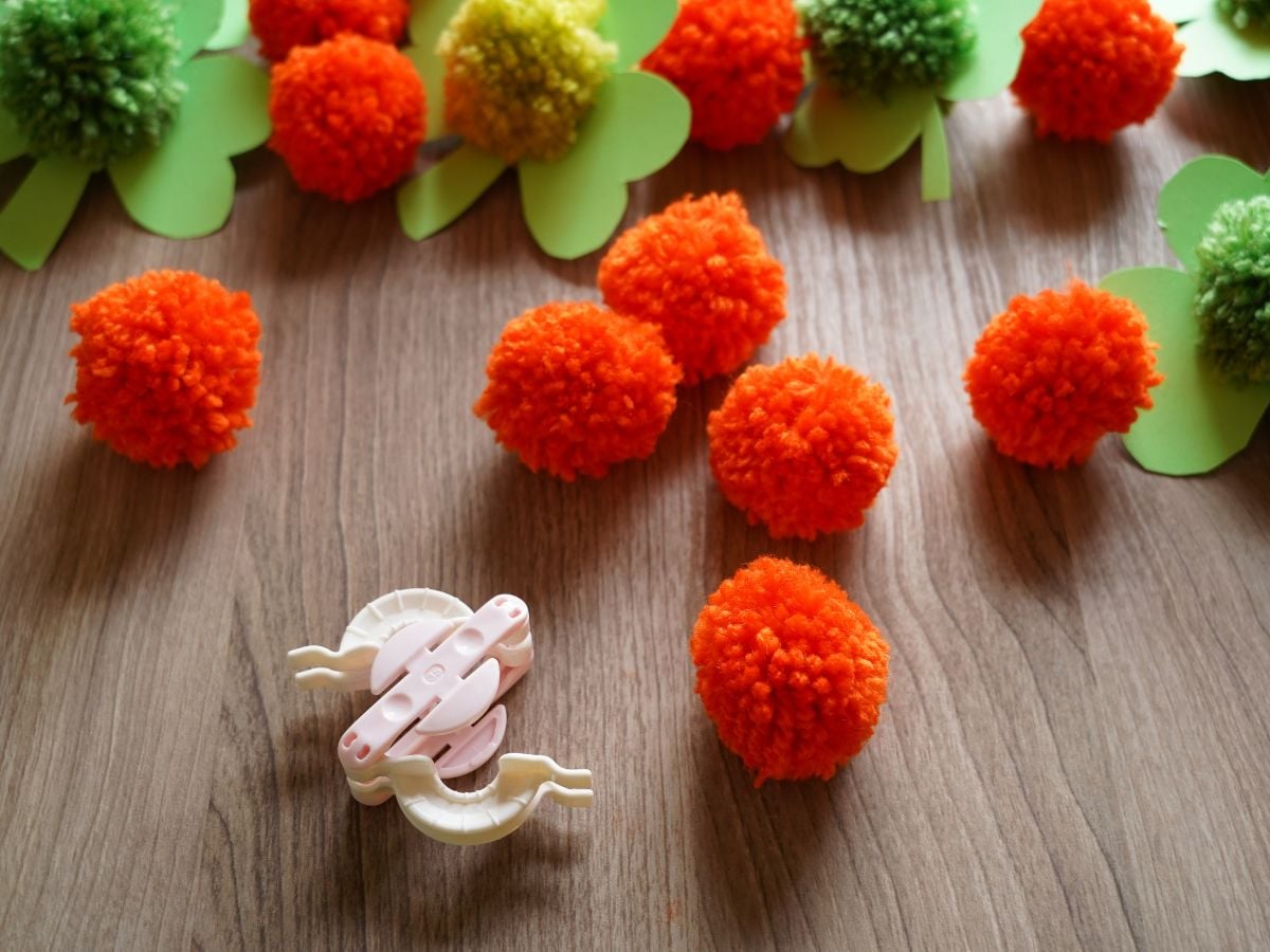 pile of orange pom pom with pom pom maker tool