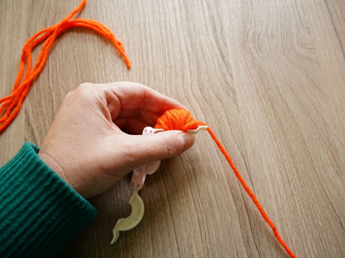 single side of pom pom maker wrapped with orange yarn in woman's hand