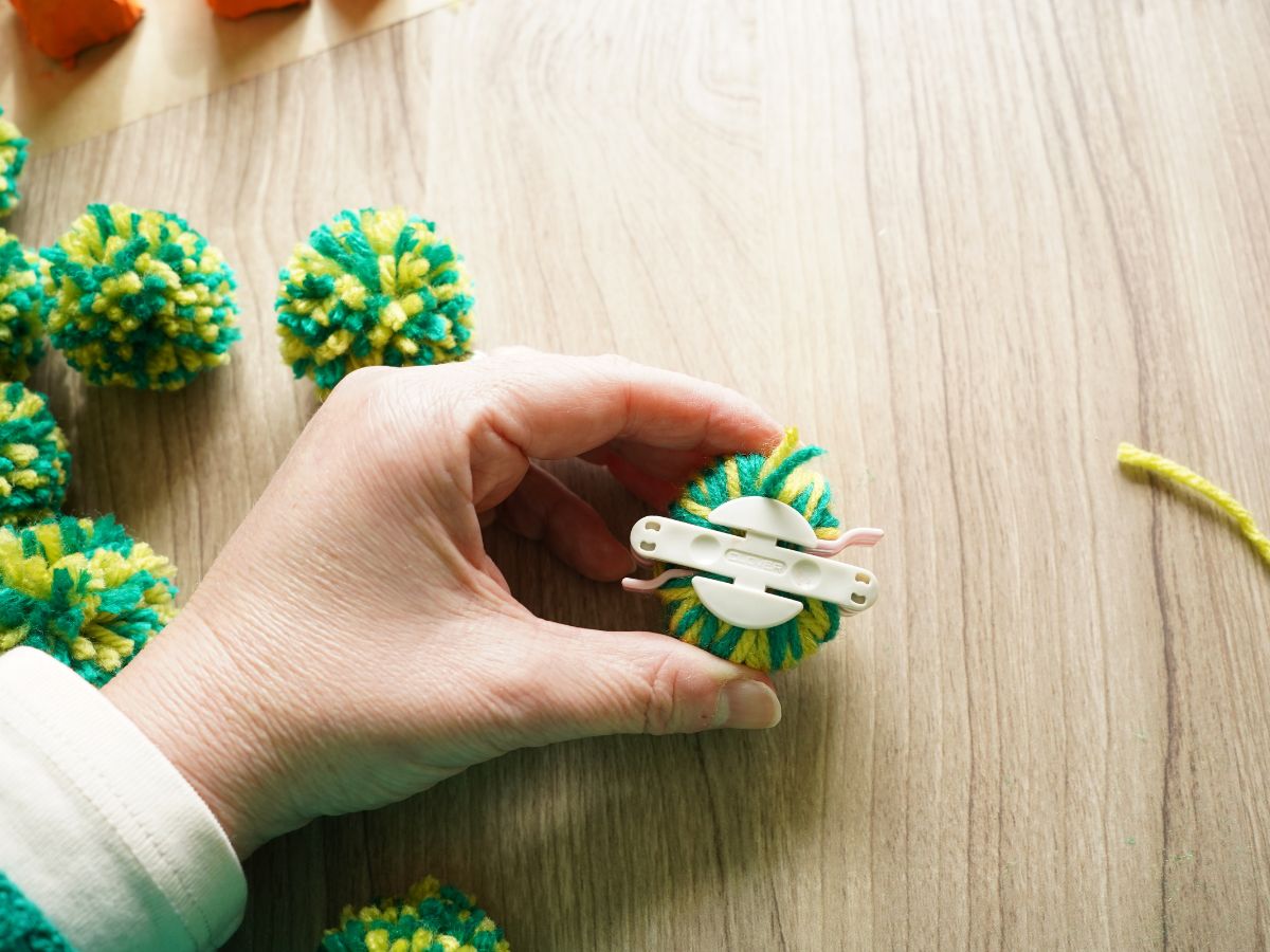 two shades of green yarn wrapped around pom pom maker tool and tool is closed held in woman's hand