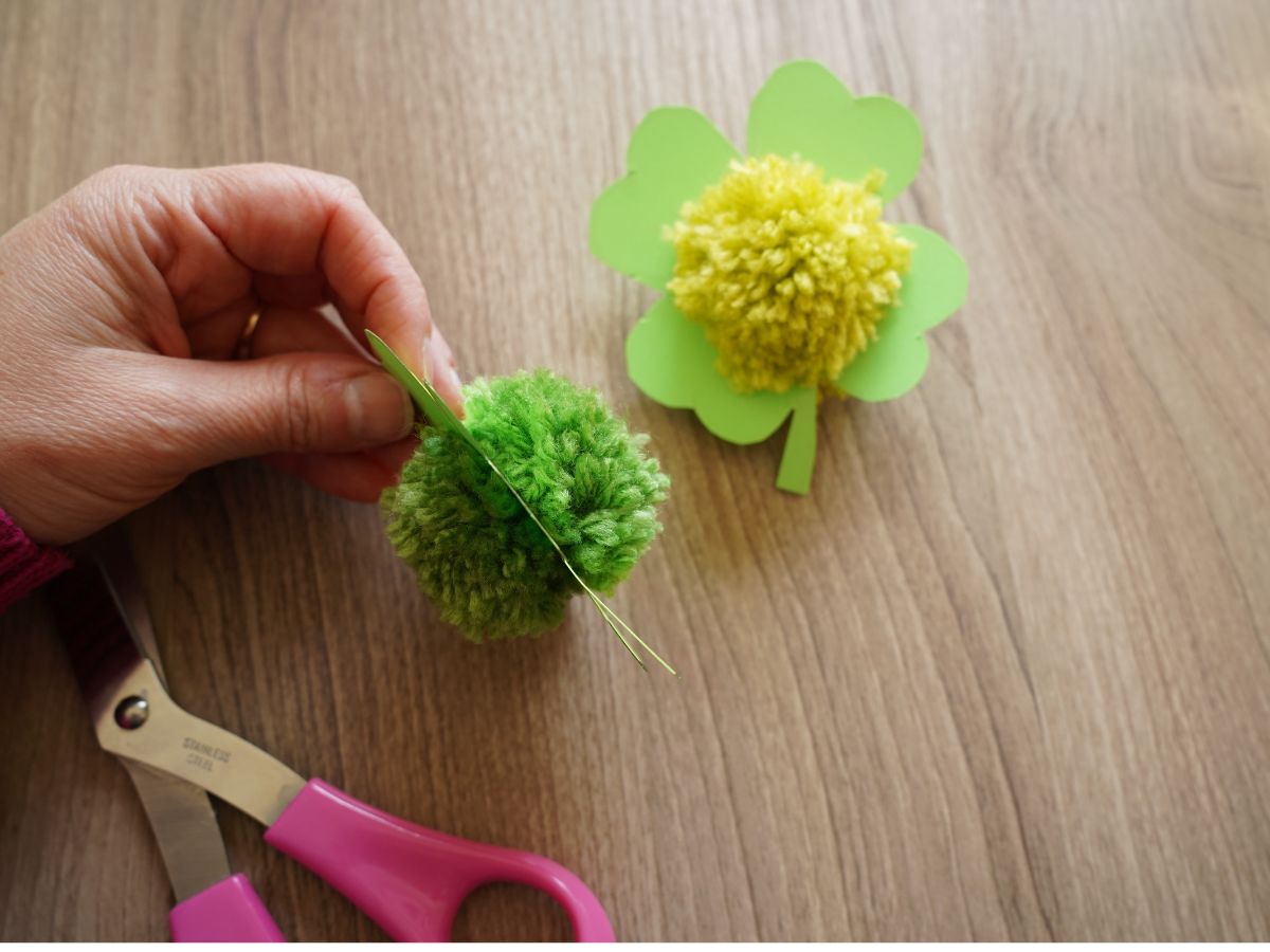 woman hand holding paper shamrock with pom pom pushed through centre