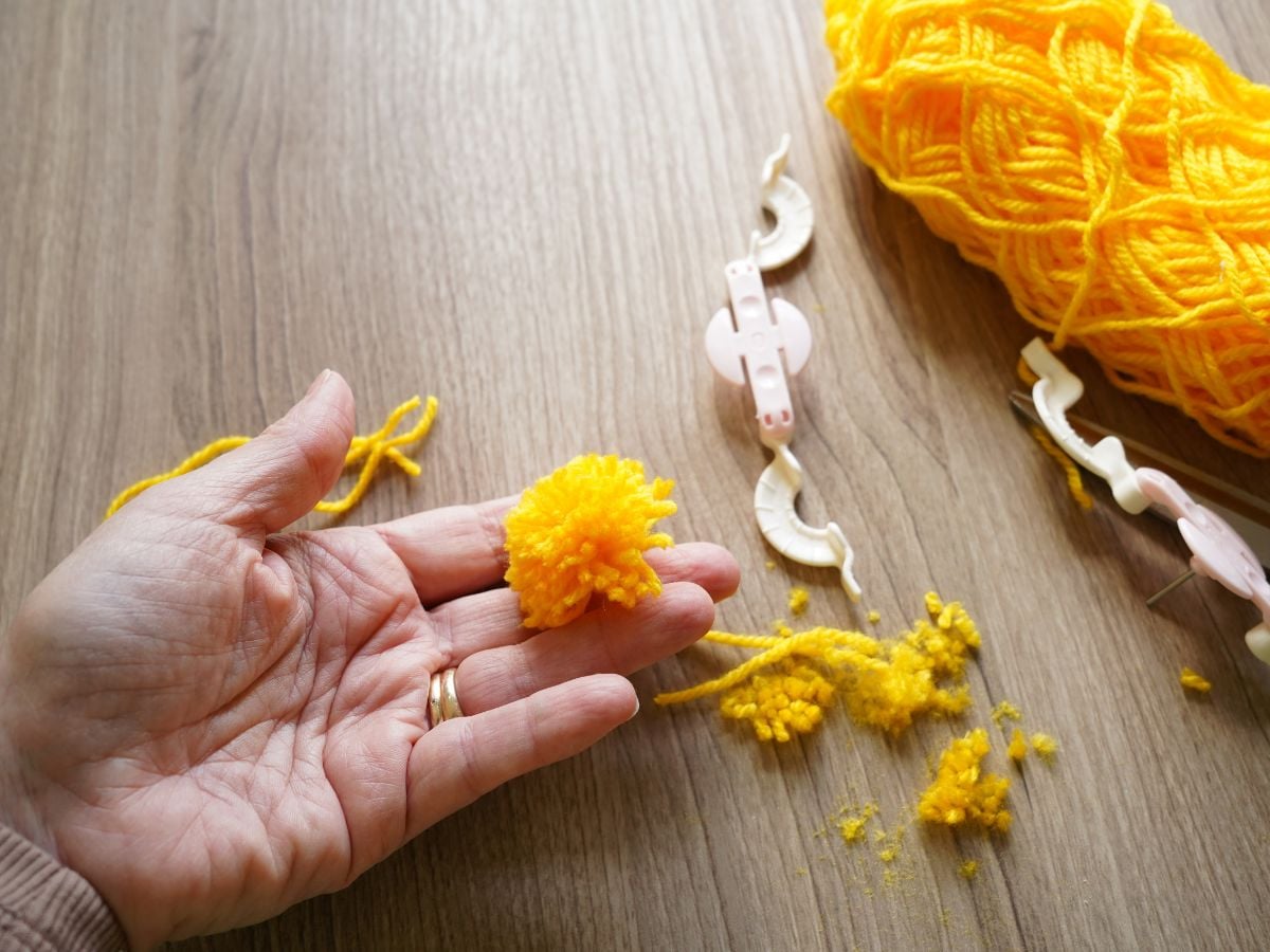 clover pom pom maker tool opened and hand holding a yellow dandelion head pom pom
