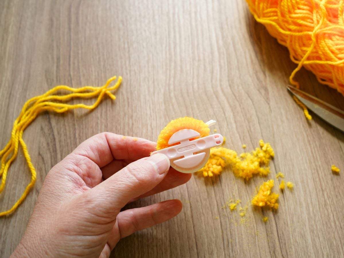 hand holding pom pom maker with trimmed yellow yarn