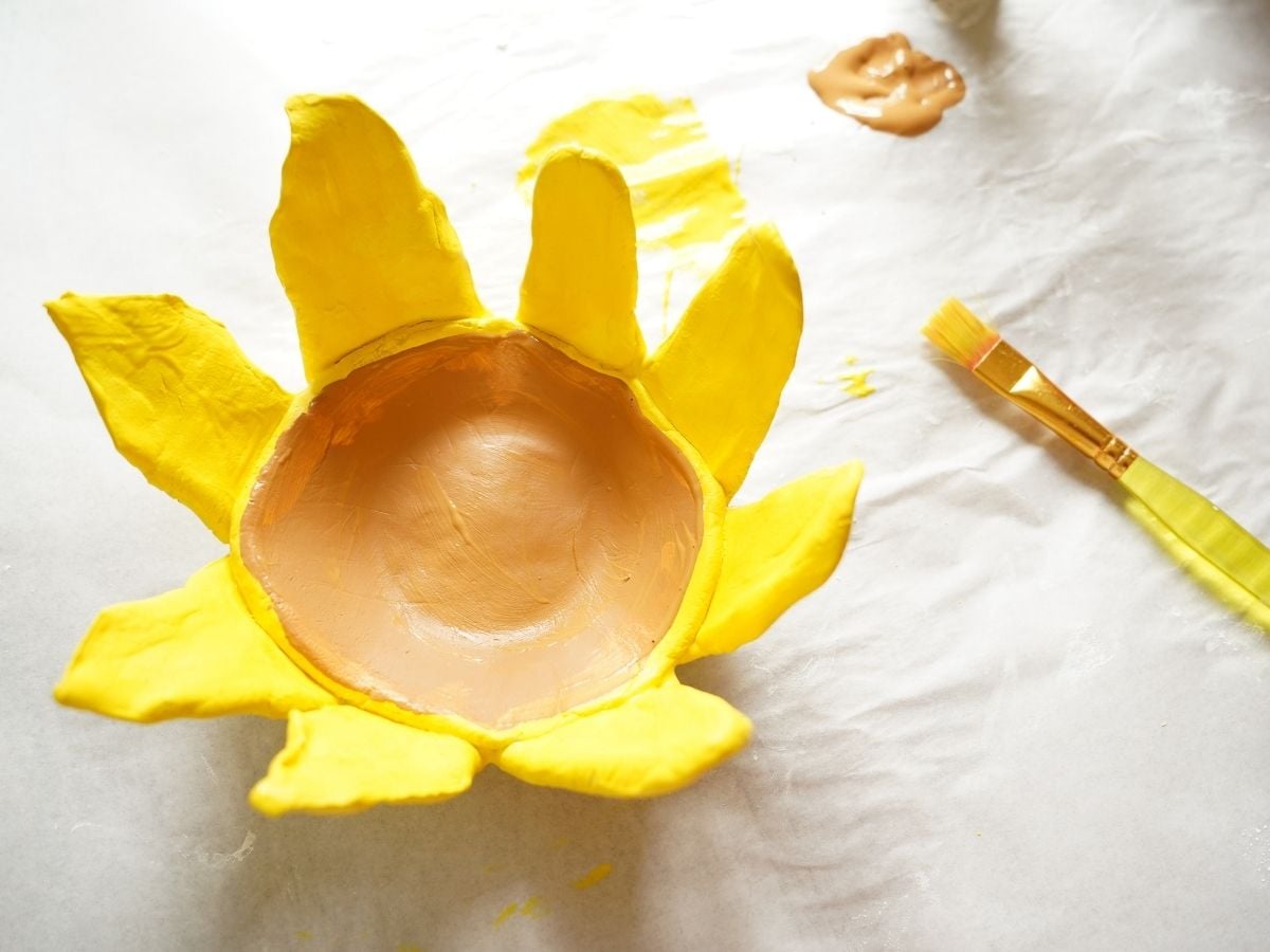 brown paint and yellow painted sunflower pinch pot with paintbrush