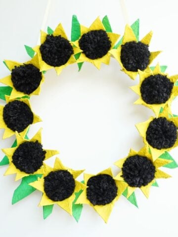 close up of egg carton sunflower wreath hanging on white wall