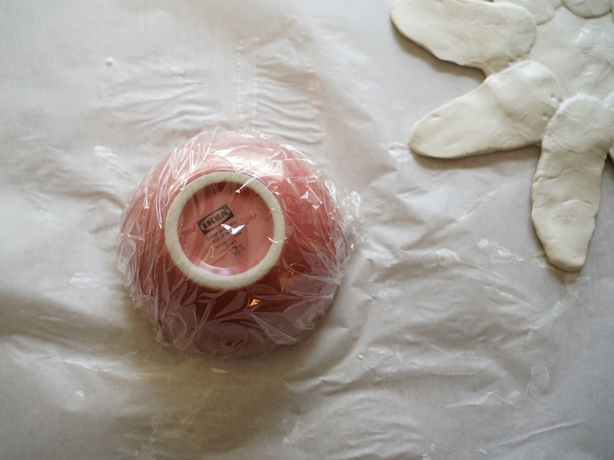 small bowl wrapped in plastic wrap sitting upside down on table for clay bowl